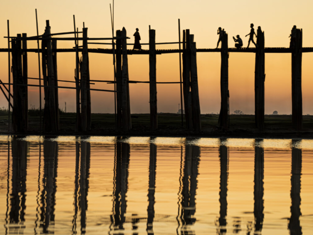 One monk, two photographers and a locals on U Bein Bridge in sunset, Amarapura, Mandalay, Myanmar (Burma)