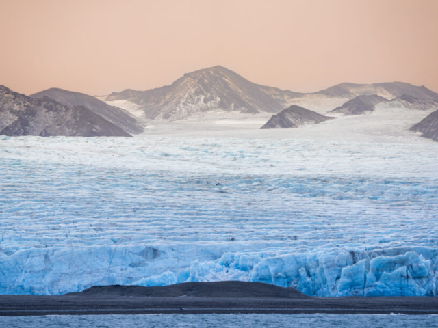 Sunrise behind mountains surrounded by massive glacier, Recherchefjorden, Wedel Jarlsberg Land, Svalbard, Norway